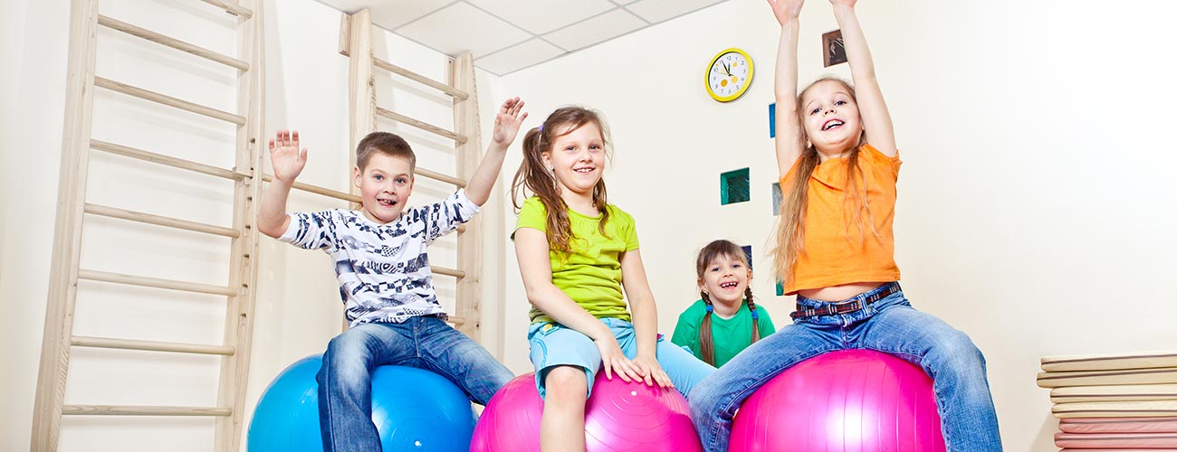 Un gruppo di bambini e bambine ognuno seduto su una palla gonfiabile in una palestra di una scuola