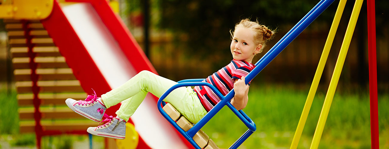 Bambina si dondola su un'altalena di metallo blu in un parco giochi