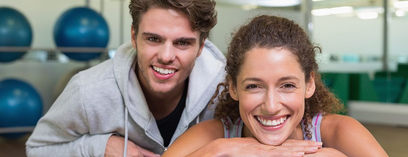 Donna riccioluta e uomo con capelli folti sorridono in una palestra