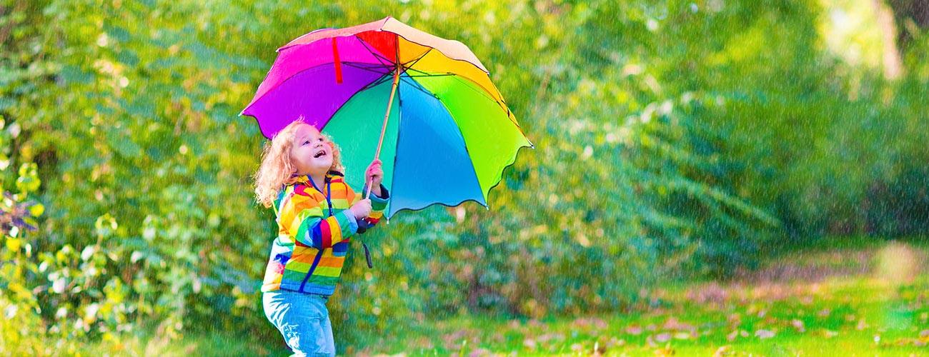 Bunt gekleidetes Mädchen mit einem Regenschirm in den Regenbogenfarben