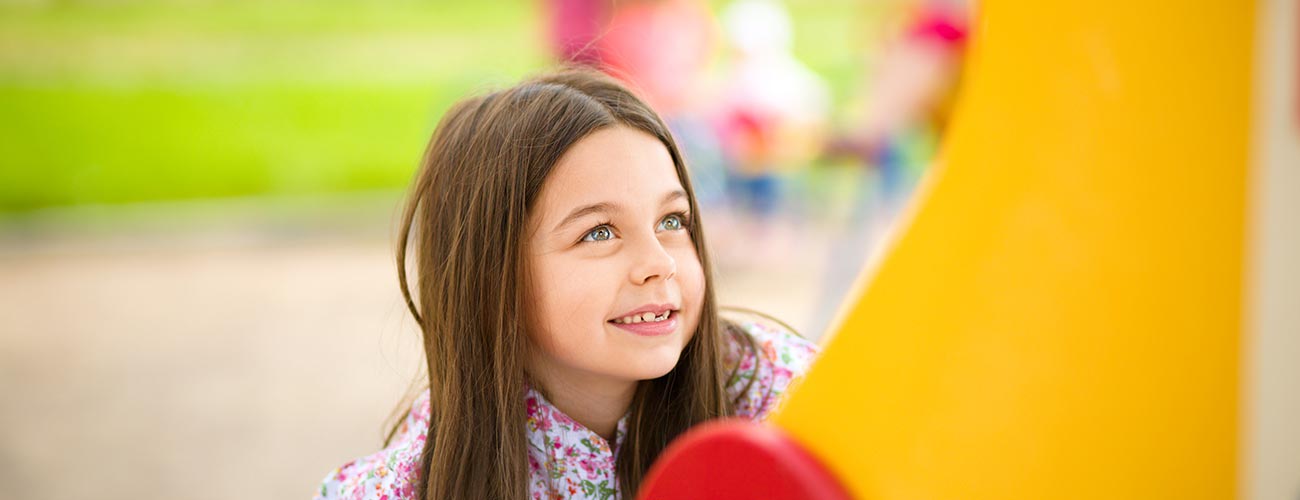 Una bambina si diverte al parco giochi giocando con uno scivolo giallo