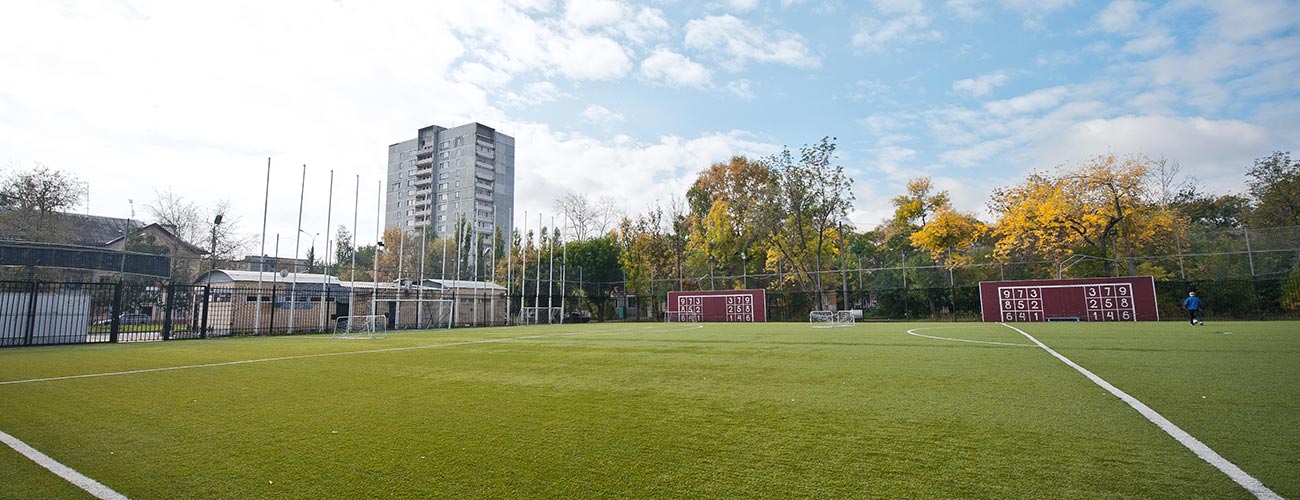 Campo da calcio posato da Ellequaranta e, sullo sfondo, palazzi alti