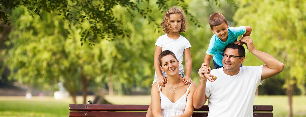Familienfoto mit Eltern und zwei Kindern auf einer Sitzbank in einem Park