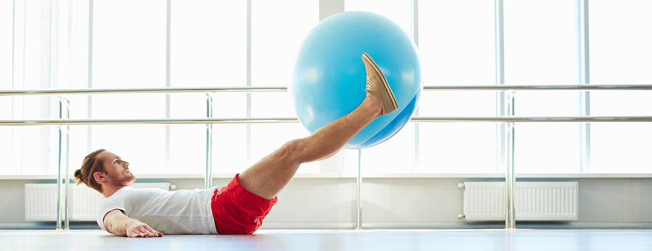 Mann beim Trainieren mit einem Sitzball, liegend auf dem Boden